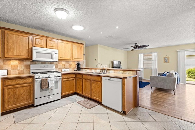 kitchen with kitchen peninsula, light tile patterned flooring, sink, and white appliances