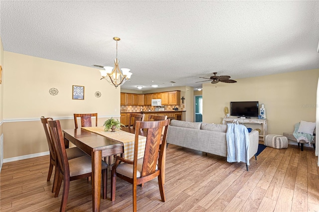 dining space with ceiling fan with notable chandelier, a textured ceiling, and light wood-type flooring