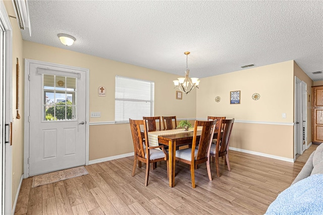 dining space with a textured ceiling, a chandelier, and light wood-type flooring