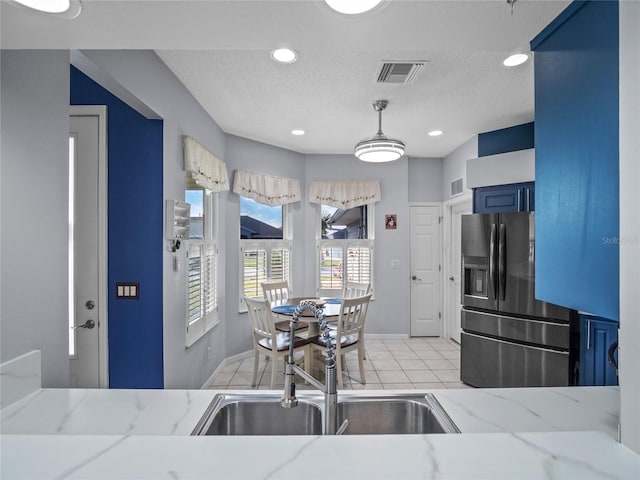 kitchen featuring stainless steel fridge with ice dispenser, light stone counters, sink, blue cabinets, and light tile patterned flooring