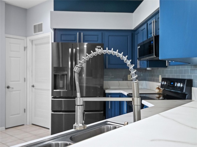 kitchen with appliances with stainless steel finishes, light tile patterned flooring, blue cabinetry, and decorative backsplash