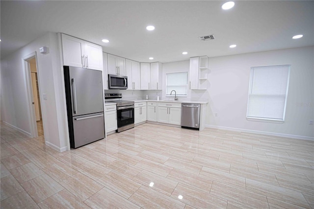 kitchen with stainless steel appliances, a sink, white cabinetry, light countertops, and open shelves