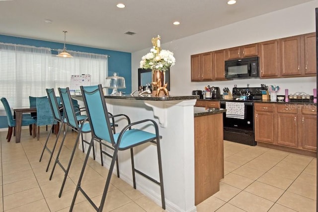 kitchen featuring a kitchen breakfast bar, hanging light fixtures, a kitchen island, light tile patterned floors, and black appliances