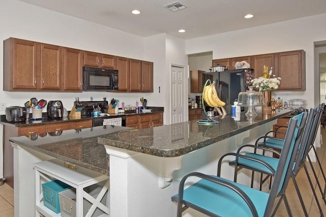 kitchen with dark stone countertops, a kitchen island, a breakfast bar area, light tile patterned floors, and black appliances