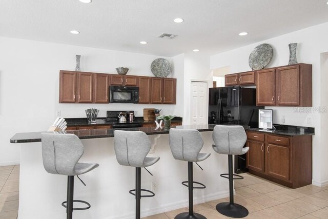 436 Orange Cosmos Blvd, Davenport, FL 33837 - kitchen with black appliances, light tile patterned flooring, dark countertops, a kitchen bar, and recessed lighting