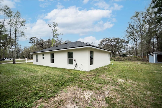 back of house featuring a storage unit, a lawn, an outdoor structure, and stucco siding