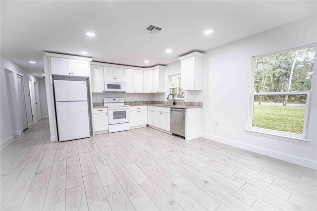 kitchen with white appliances, visible vents, white cabinets, light wood-style flooring, and a sink