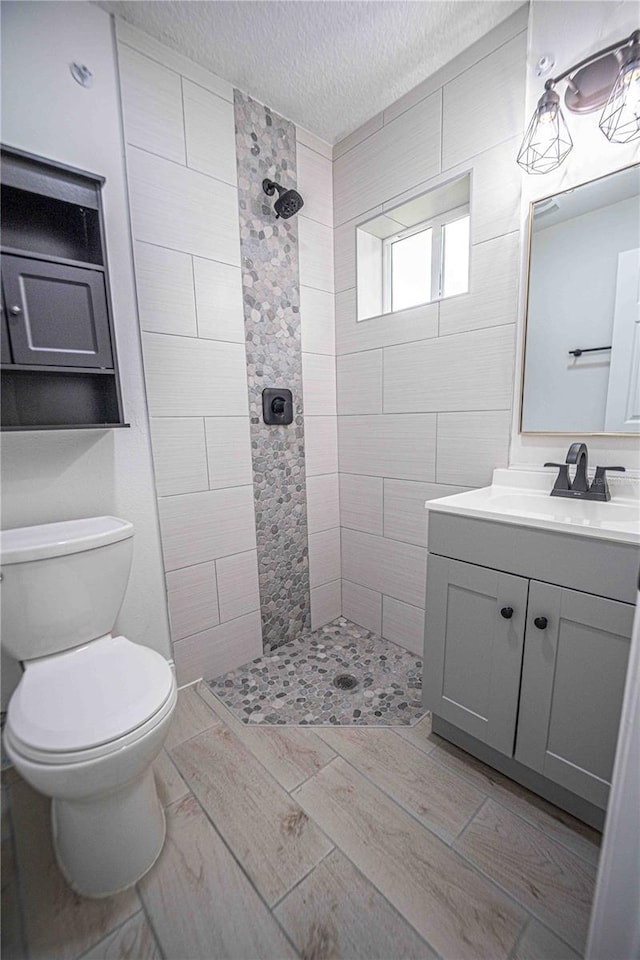 bathroom featuring a walk in shower, toilet, a textured ceiling, and vanity