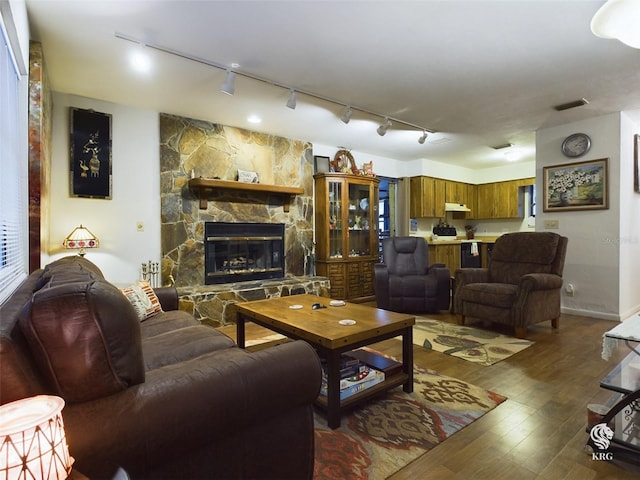 living room featuring track lighting, hardwood / wood-style floors, and a stone fireplace