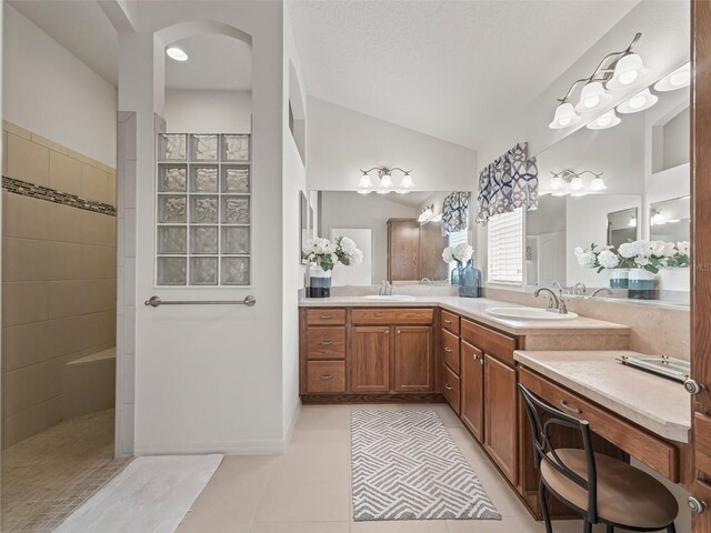 bathroom featuring vanity, a textured ceiling, a tile shower, tile patterned floors, and vaulted ceiling