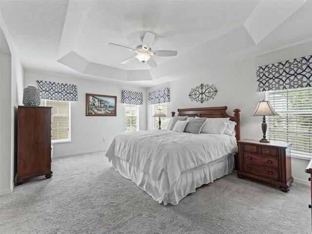 bedroom with ceiling fan, a tray ceiling, and multiple windows