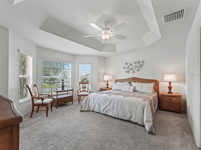 carpeted bedroom with ceiling fan, a textured ceiling, and a tray ceiling