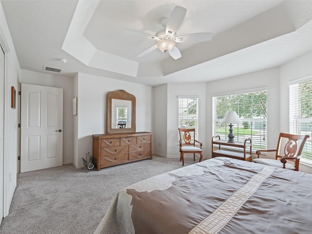 bedroom with ceiling fan, light colored carpet, a raised ceiling, and multiple windows