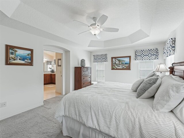 carpeted bedroom featuring ensuite bath, ceiling fan, a raised ceiling, and a textured ceiling