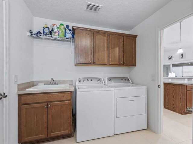 washroom featuring cabinets, a textured ceiling, sink, light tile patterned floors, and separate washer and dryer