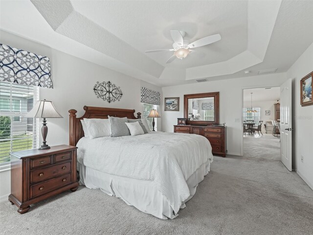 bedroom with a tray ceiling, ceiling fan, and light carpet