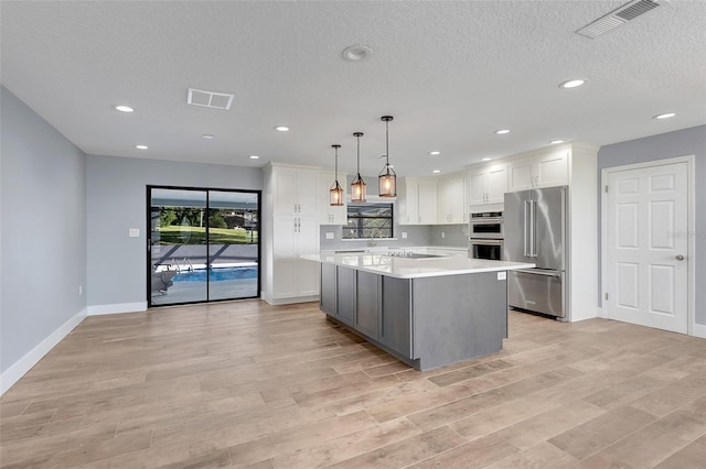 kitchen featuring hanging light fixtures, light hardwood / wood-style flooring, white cabinetry, stainless steel appliances, and a center island