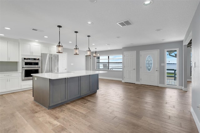 kitchen with a spacious island, white cabinets, stainless steel appliances, and decorative light fixtures