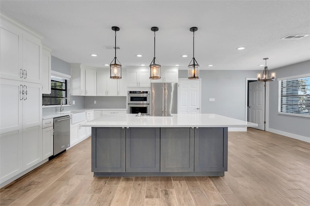 kitchen featuring a large island with sink, decorative light fixtures, stainless steel appliances, and plenty of natural light