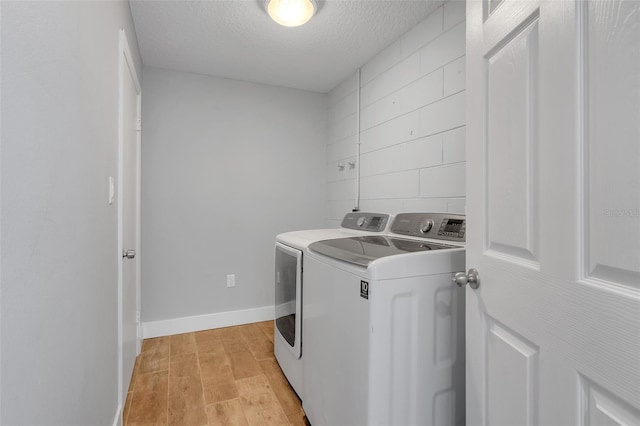 laundry area with light wood-type flooring, washer and clothes dryer, and a textured ceiling