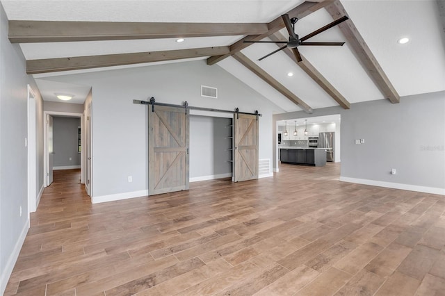 unfurnished living room with a barn door, vaulted ceiling with beams, ceiling fan, and light hardwood / wood-style flooring