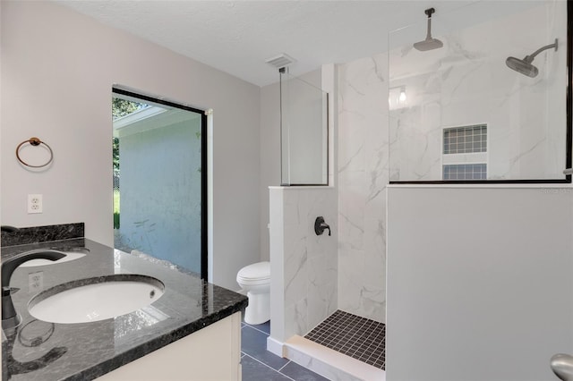 bathroom with tile patterned flooring, tiled shower, vanity, and toilet