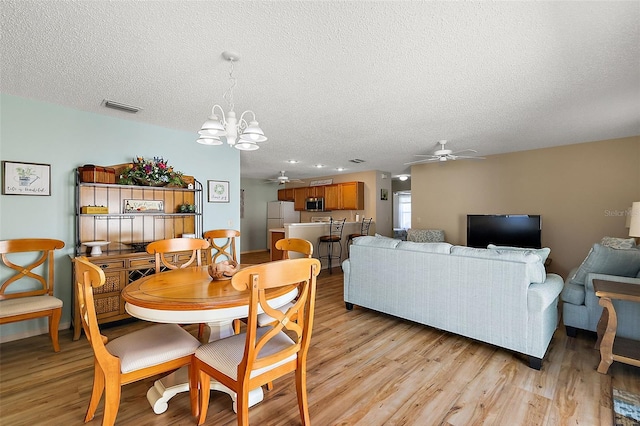 dining space featuring a textured ceiling, ceiling fan with notable chandelier, and light hardwood / wood-style flooring