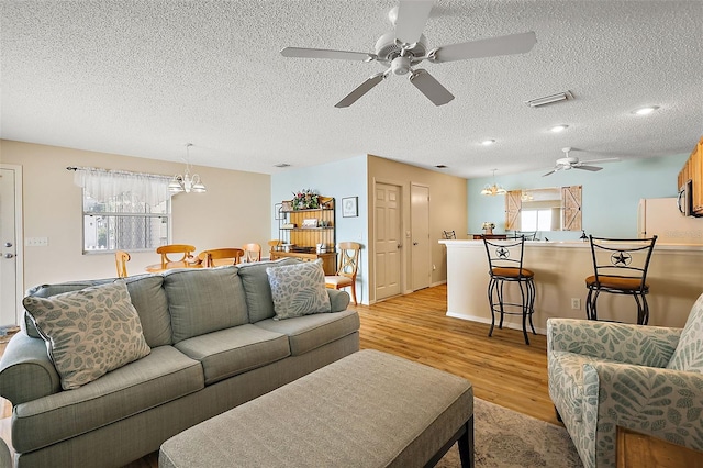 living room with ceiling fan with notable chandelier, a wealth of natural light, light hardwood / wood-style floors, and a textured ceiling