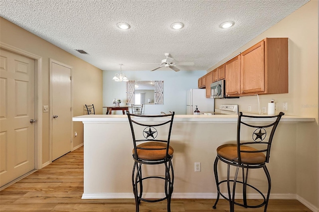 kitchen with ceiling fan with notable chandelier, white appliances, kitchen peninsula, a breakfast bar area, and light wood-type flooring