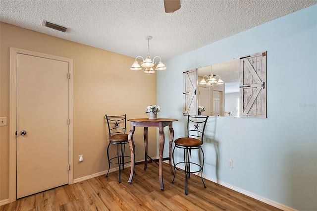 dining room with a textured ceiling, wood-type flooring, and a chandelier