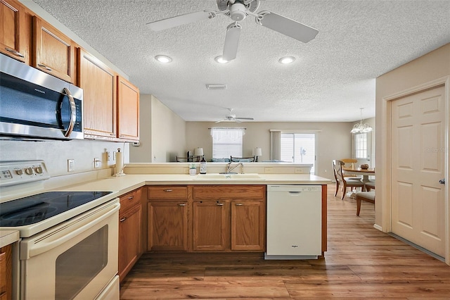 kitchen with dark wood-type flooring, ceiling fan with notable chandelier, white appliances, kitchen peninsula, and sink