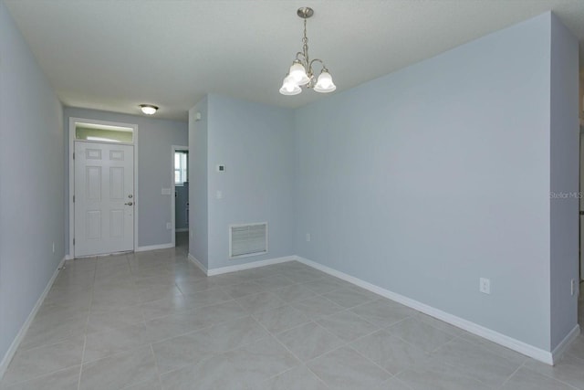 tiled spare room with a notable chandelier