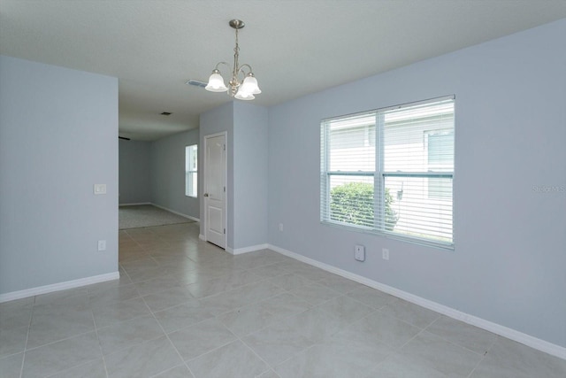 tiled spare room featuring a chandelier