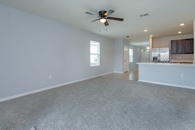 unfurnished living room featuring light carpet, ceiling fan, and sink