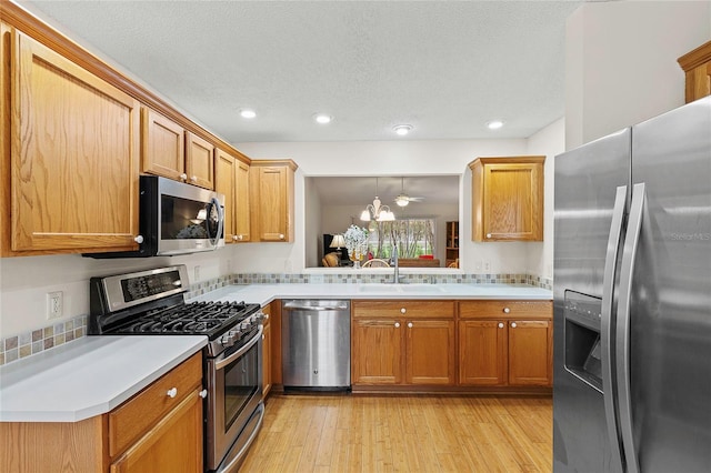 kitchen featuring a textured ceiling, appliances with stainless steel finishes, sink, and light hardwood / wood-style flooring