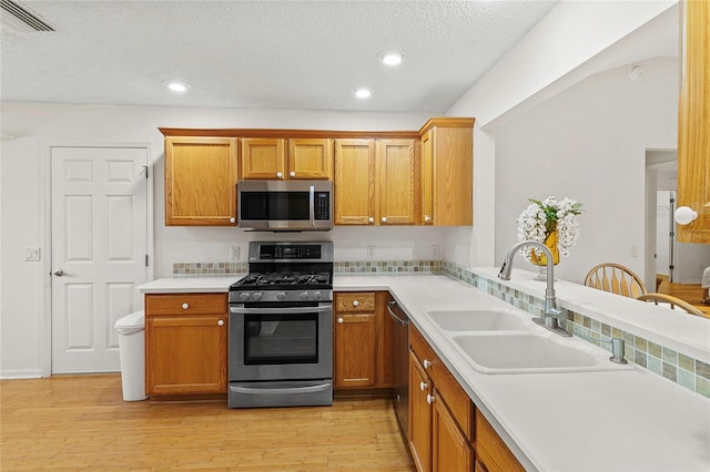 kitchen with light wood-type flooring, appliances with stainless steel finishes, a textured ceiling, sink, and kitchen peninsula