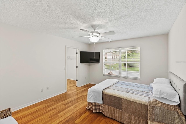 bedroom with a textured ceiling, light hardwood / wood-style flooring, ceiling fan, and a spacious closet