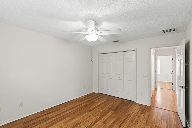 unfurnished bedroom with a closet, wood-type flooring, ceiling fan, and a textured ceiling