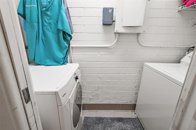 clothes washing area featuring washing machine and dryer and brick wall