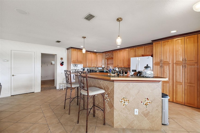 kitchen with hanging light fixtures, a kitchen island, white refrigerator with ice dispenser, a breakfast bar area, and light tile patterned floors