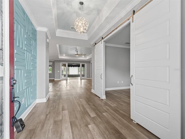 foyer with a barn door, a raised ceiling, ceiling fan with notable chandelier, and hardwood / wood-style flooring