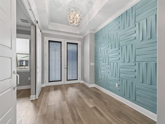 foyer with a barn door, wood-type flooring, crown molding, a tray ceiling, and a chandelier