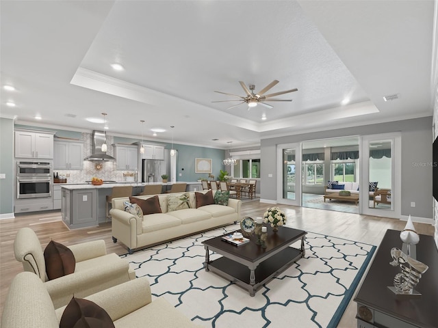 living room featuring ceiling fan, a tray ceiling, light wood-type flooring, and ornamental molding