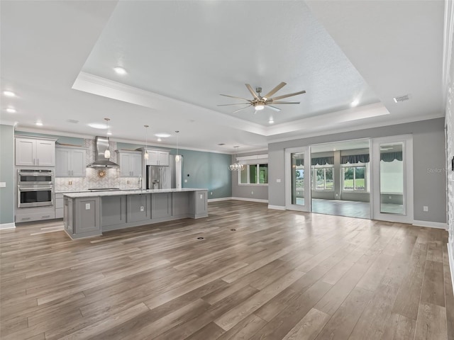 unfurnished living room featuring light wood-type flooring, crown molding, a tray ceiling, and ceiling fan