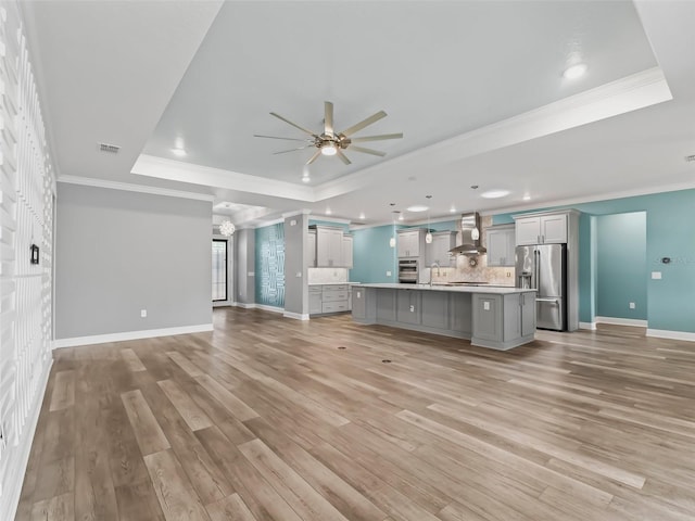 unfurnished living room with light wood-type flooring, a raised ceiling, ceiling fan with notable chandelier, and crown molding