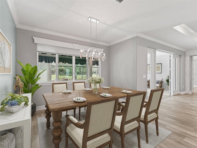 dining area with light hardwood / wood-style floors, ornamental molding, and an inviting chandelier