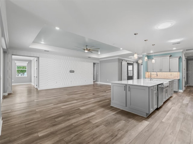 kitchen with ceiling fan, gray cabinetry, a kitchen island with sink, a tray ceiling, and light hardwood / wood-style floors