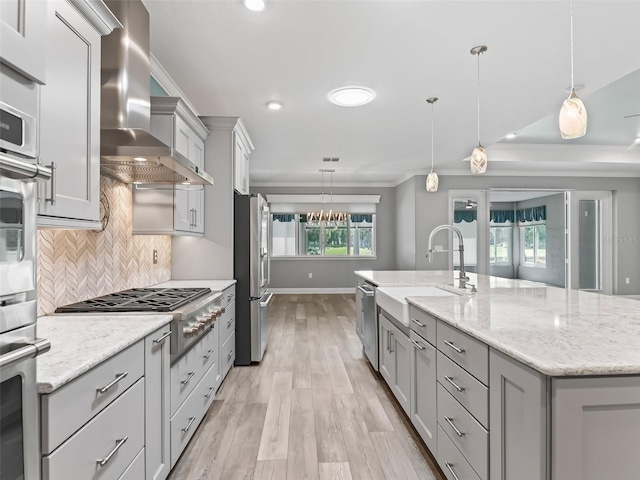 kitchen with light wood-type flooring, hanging light fixtures, wall chimney exhaust hood, and a kitchen island with sink