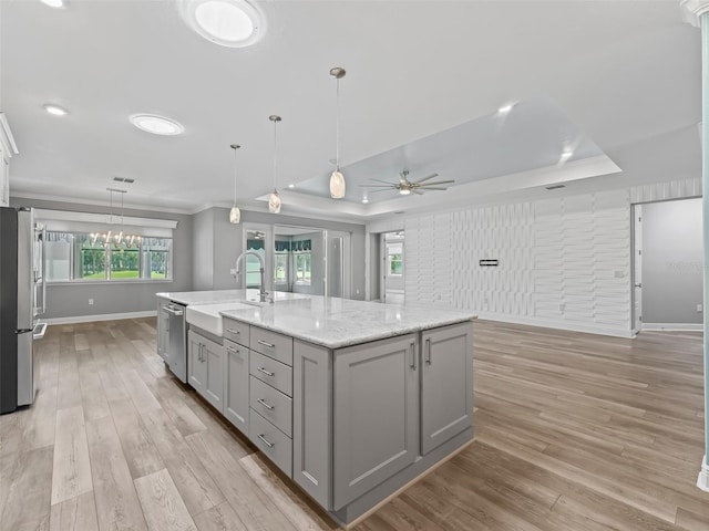 kitchen featuring appliances with stainless steel finishes, a large island with sink, ceiling fan with notable chandelier, gray cabinets, and sink