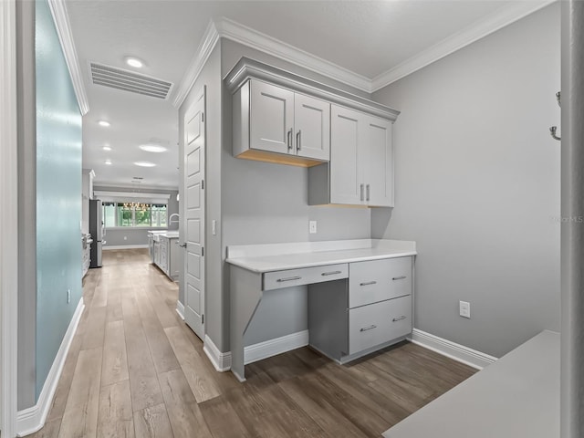 kitchen featuring gray cabinets, dark hardwood / wood-style floors, built in desk, and crown molding